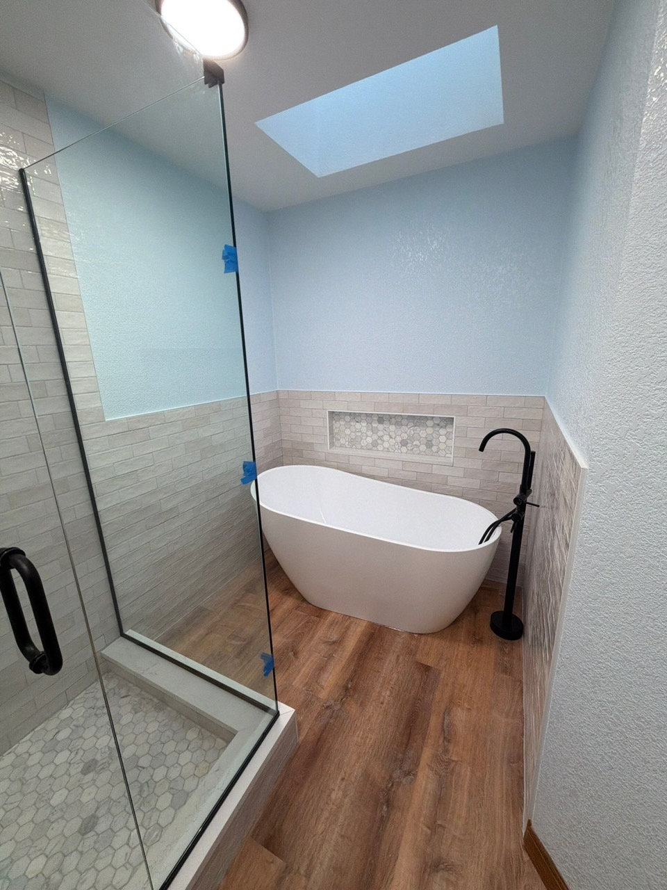 Freestanding tub remodel with wood look flooring and bathroom wall tile