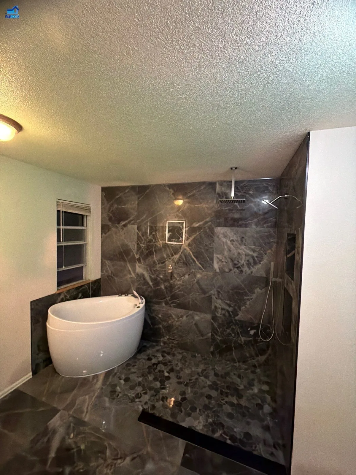 Dark natural-stone bathroom with a freestanding soaking tub and ceiling-mount rain shower head